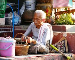 Elderly local women cooking on her front steps for a restaurant located across the street. Luang Prabang, Laos.