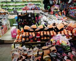 A vendor at the market. Notice the mannequin feet for displaying the shoes. Inventory is always stacked tall with just enough room to walk down aisles. Pakse, Laos.